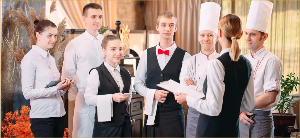 Команда ресторану з шести осіб стоїть у колі під час наради. Два шеф-кухарі в білих кухарських ковпаках уважно слухають співробітника.
